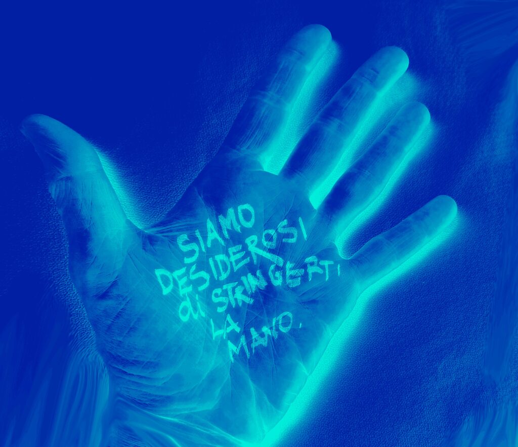 Foto di un amano con un filtro blu, aperta con il palmo rivolto allo schermo. Sul palmo c'è una scritta che dice: "Siamo desiderosi di stringerti la mano."